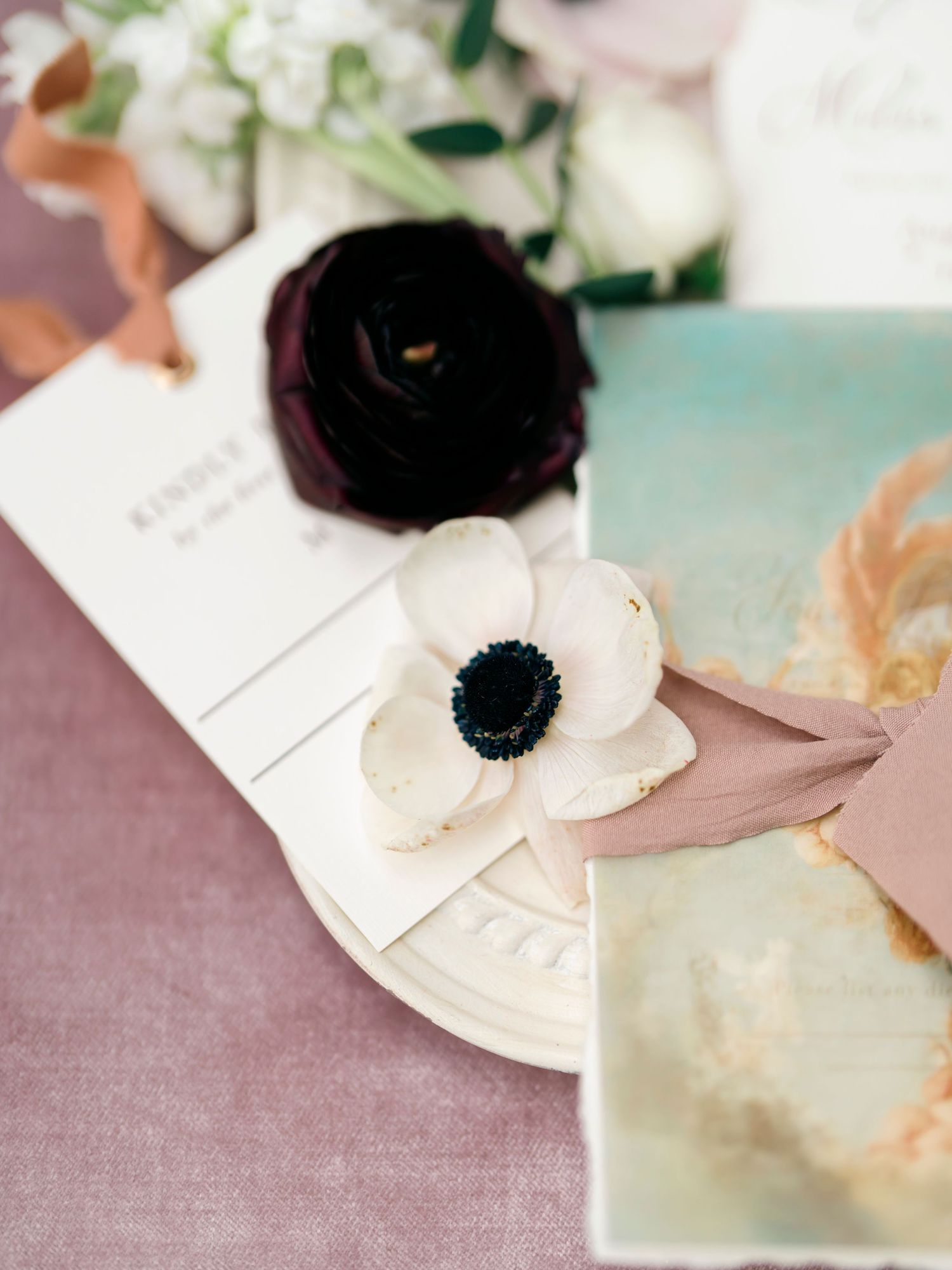 Wedding stationery detail with black and white anemone flowers on blush pink background.