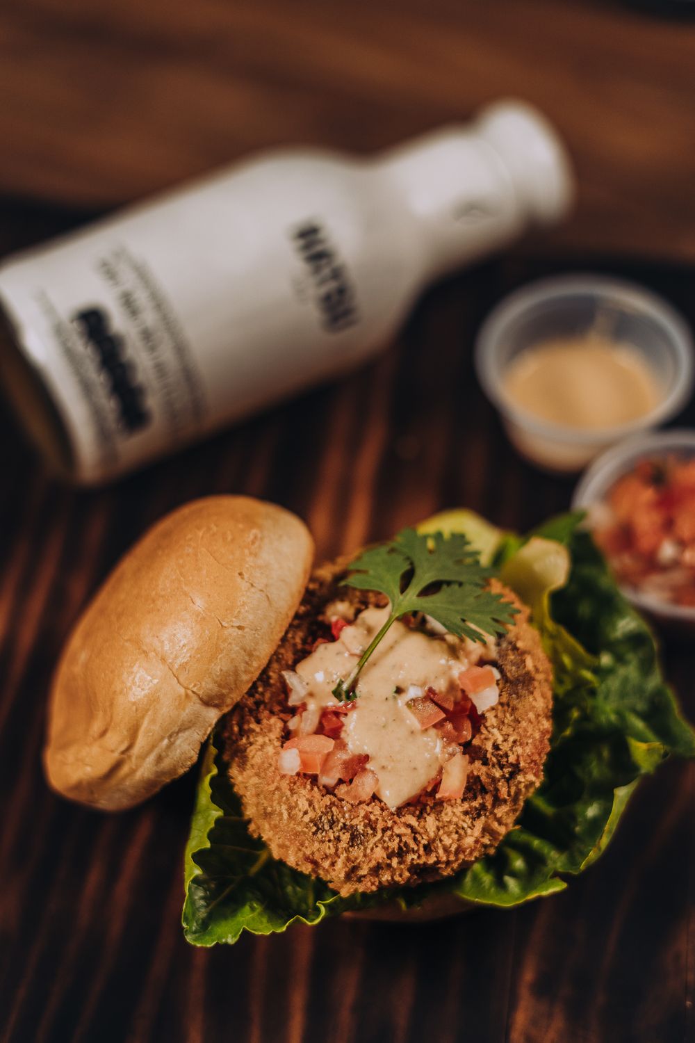 A crispy breaded sandwich topped with fresh herbs and sauce on a wooden surface.