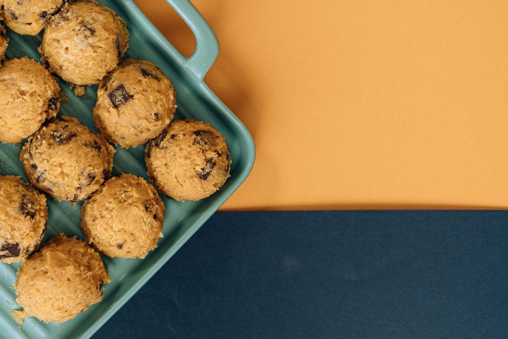 Fresh chocolate chip cookies cooling in a turquoise baking dish on orange and navy background.