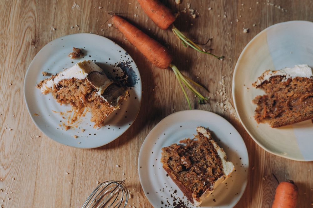 Sliced carrot cake pieces on plates with fresh carrots on wooden surface.
