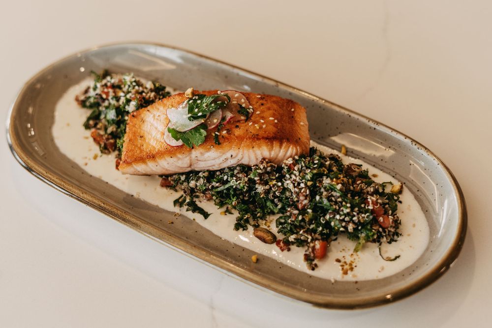 Pan-seared salmon served alongside quinoa tabbouleh on an oval ceramic plate.