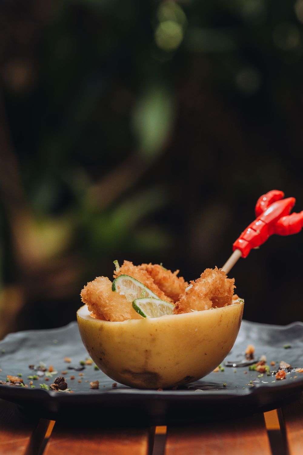 Breaded shrimp appetizer served in melon bowl with lime garnish on black plate.