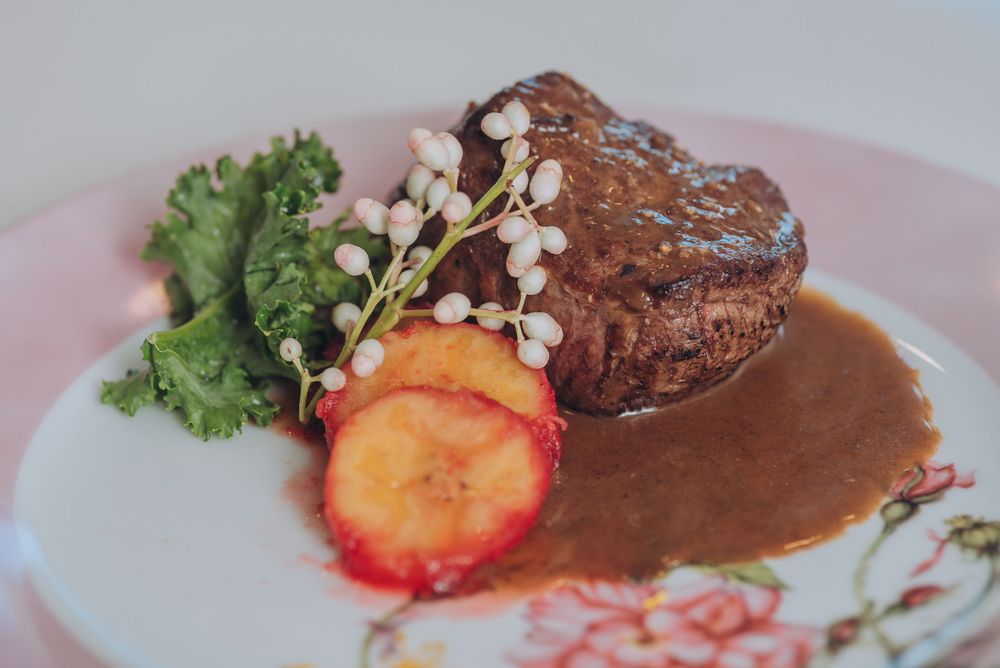 Grilled steak with sauce and garnished with fresh herbs and strawberry on pink plate.
