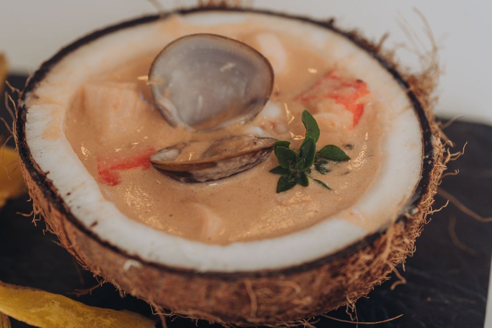 Seafood soup served in a fresh coconut bowl with shellfish and herbs.