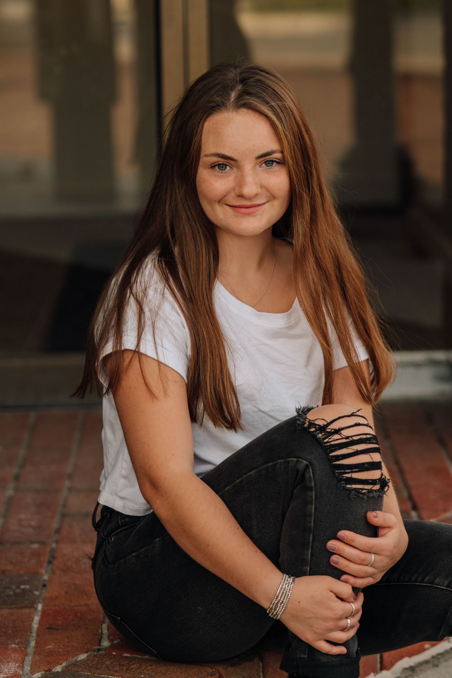 Person in casual white t-shirt and black jeans sitting on brick pavement.