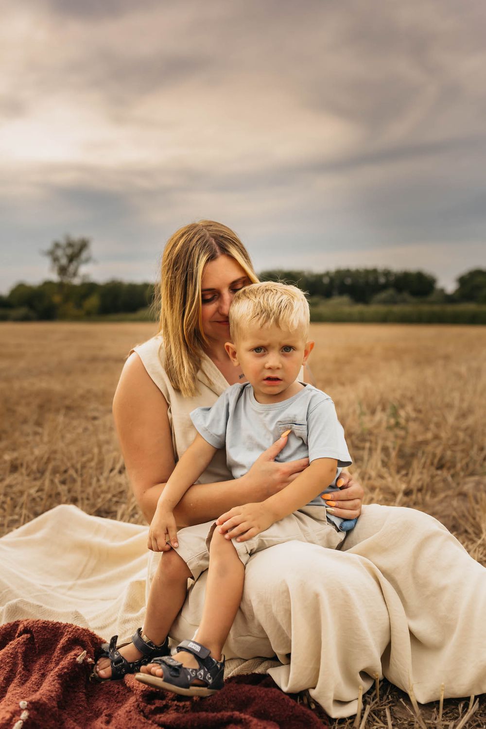Mother and young child sharing an intimate moment while sitting on blankets in a wheat field.