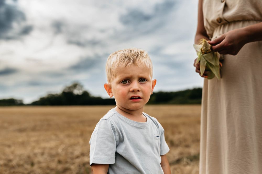 Young child stands in a harvested field wearing a gray t-shirt on an overcast day.