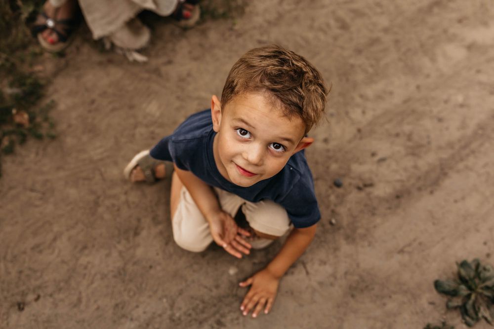 Young child playing in dirt and smiling at camera from ground level.
