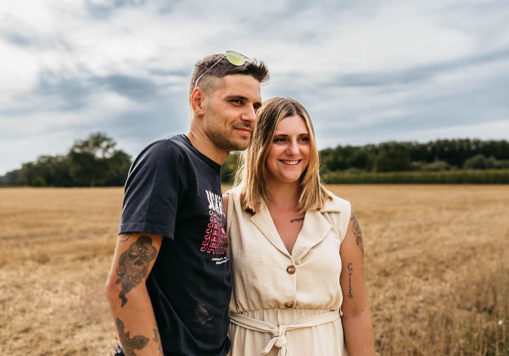 Couple standing together in wheat field on cloudy summer day.
