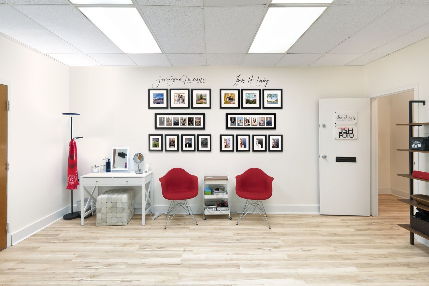 Modern studio waiting area with red chairs, framed artwork, and minimalist decor on white walls.