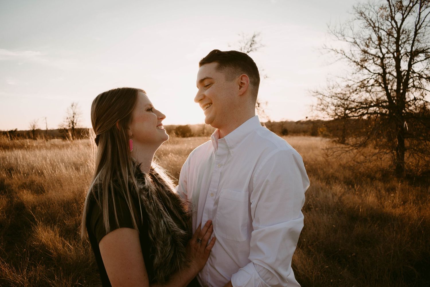 A couple shares an intimate moment while standing in a field at sunset.