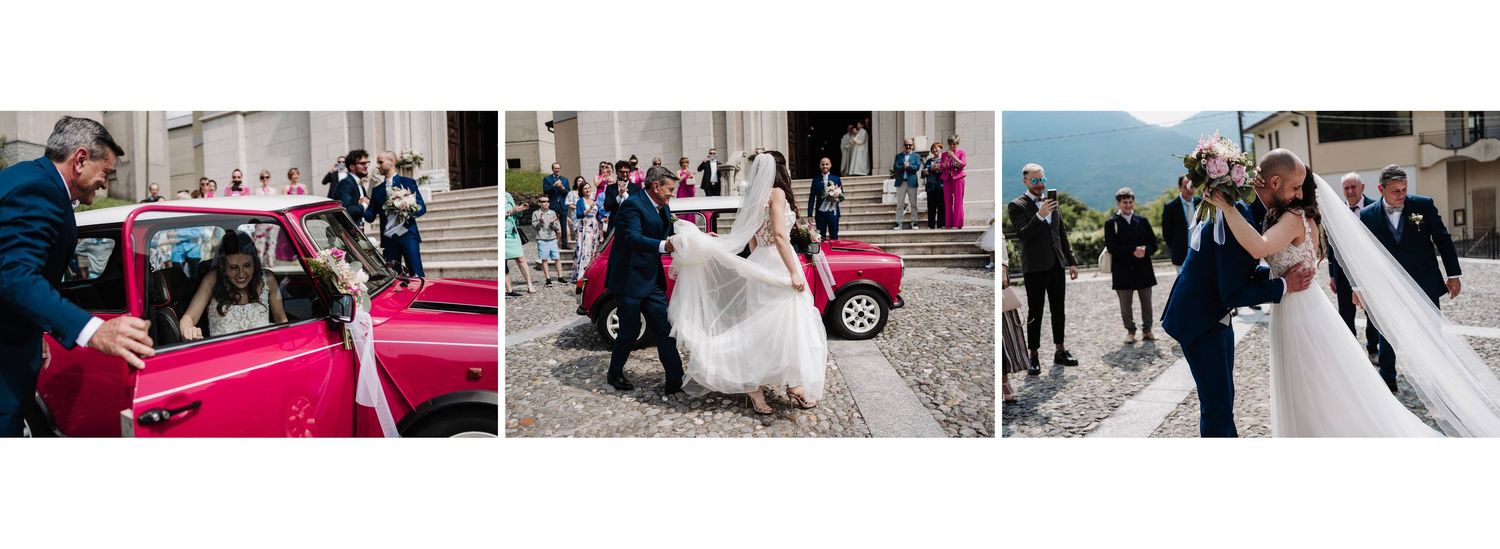 Joyful wedding ceremony exit with bride and groom beside vintage red car outside historic stone church.
