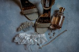 Wedding accessories including perfume bottle, garter, and jewelry arranged on blue surface.