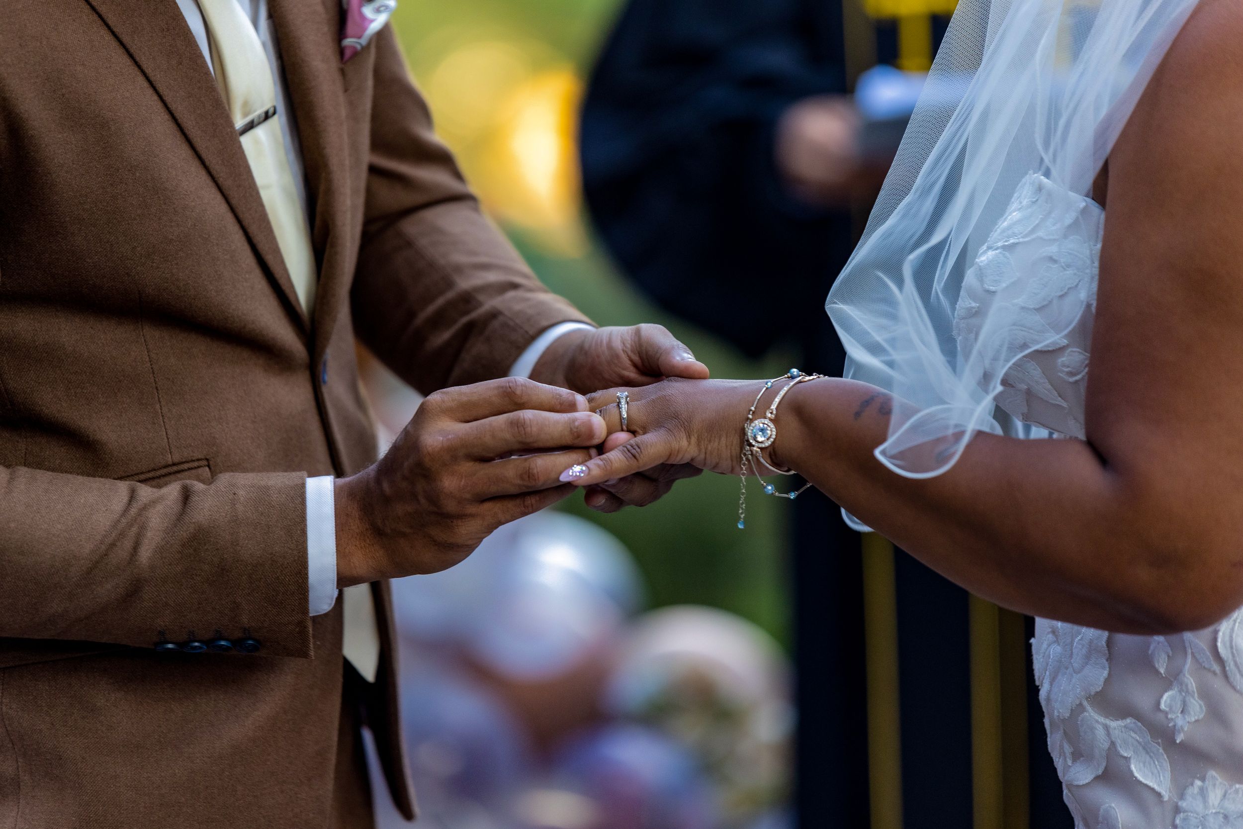 Close-up of wedding ring exchange during outdoor ceremony.