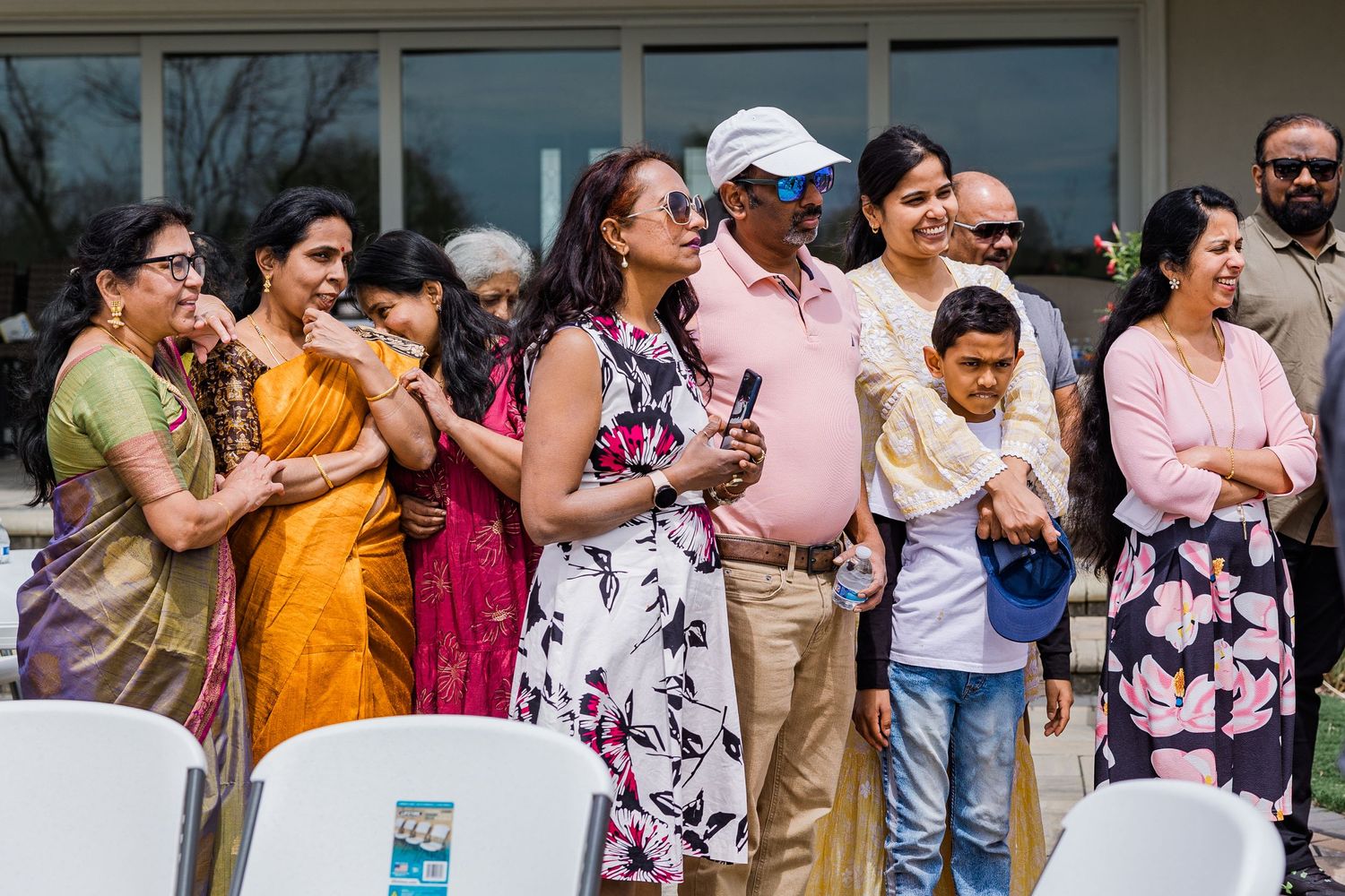 A group of people in colorful traditional Indian attire watch and smile during an outdoor celebration.