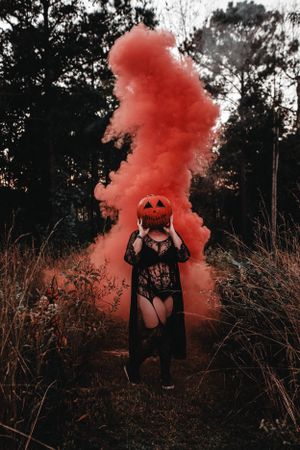 Atmospheric Halloween scene with a pumpkin mask and red smoke bomb in a moody forest setting. spooky, horror, pumpkin