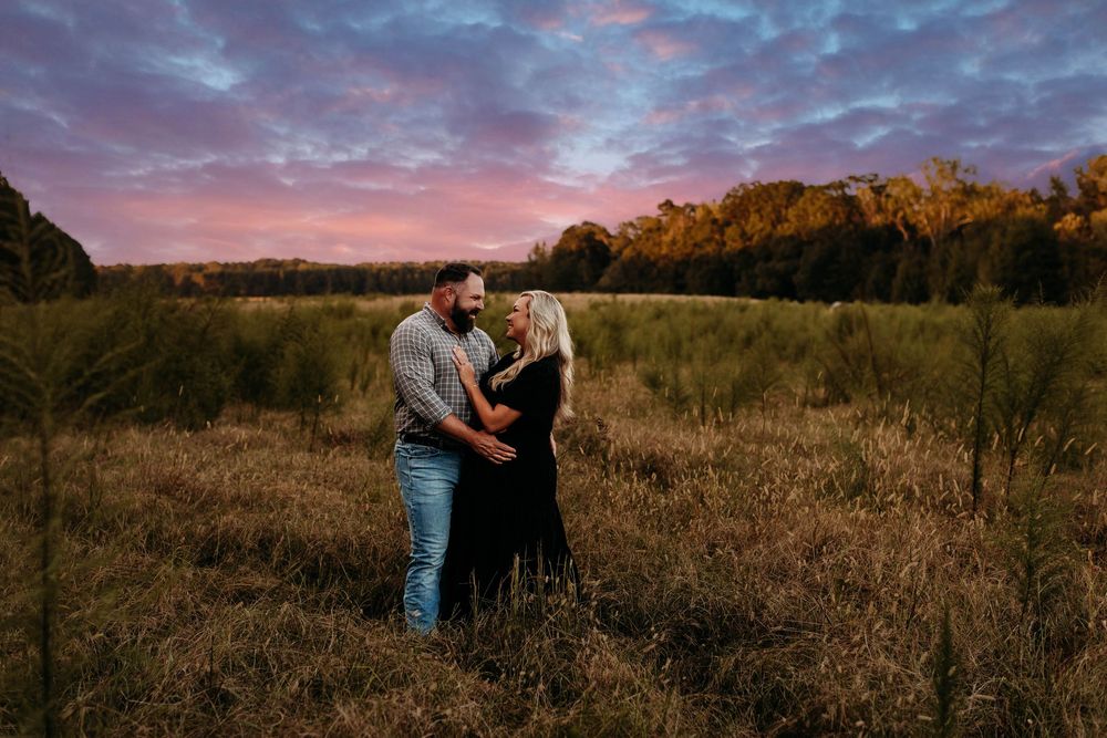 A couple shares an intimate moment in a golden field during sunset as warm light illuminates the autumn landscape.