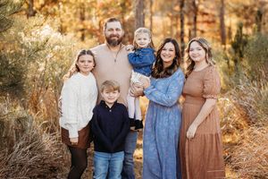 Family of six posing outdoors in fall foliage, parents with four children smiling in coordinated earth-tone outfits.