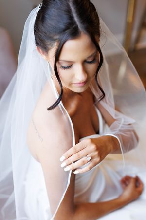 A bride in a white veil and robe gazes down while getting ready on her wedding day.