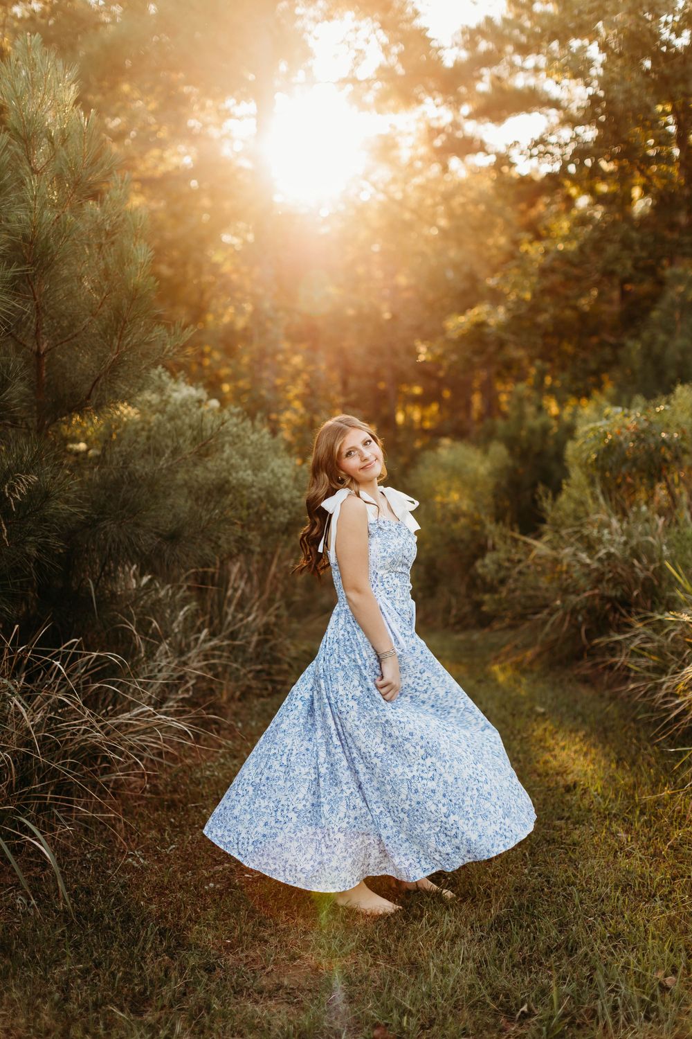 A young girl in a blue floral dress twirls in a sunlit meadow during golden hour.