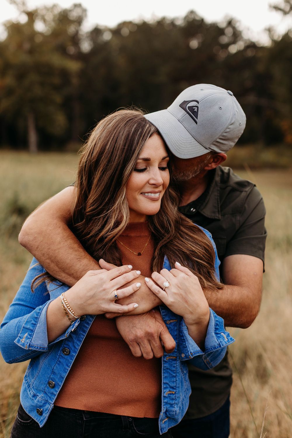 A couple embraces in a golden field wearing denim and casual attire during a romantic outdoor photo session.