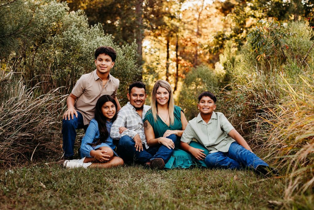 Family members lounging together on grass during golden hour autumn photoshoot in a natural outdoor setting.