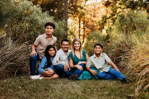 Family members lounging together on grass during golden hour autumn photoshoot in a natural outdoor setting.