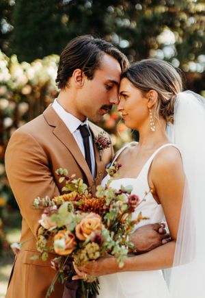 A romantic moment captured between newlyweds with autumn floral bouquet in warm sunlit outdoor setting. fall wedding, wedding photography
