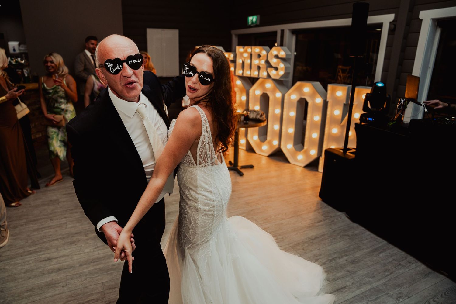 Wedding couple dances together near illuminated marquee letters during evening reception.