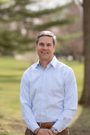 Professional outdoor portrait of someone in a light blue dress shirt and brown belt standing in a natural setting.