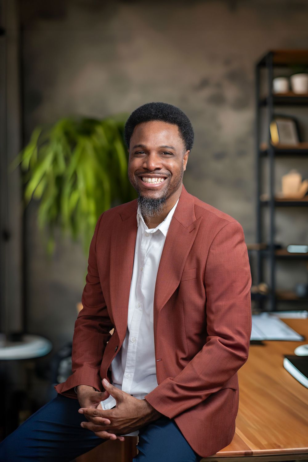 Warm professional portrait in rust colored blazer with genuine smile in modern office setting.