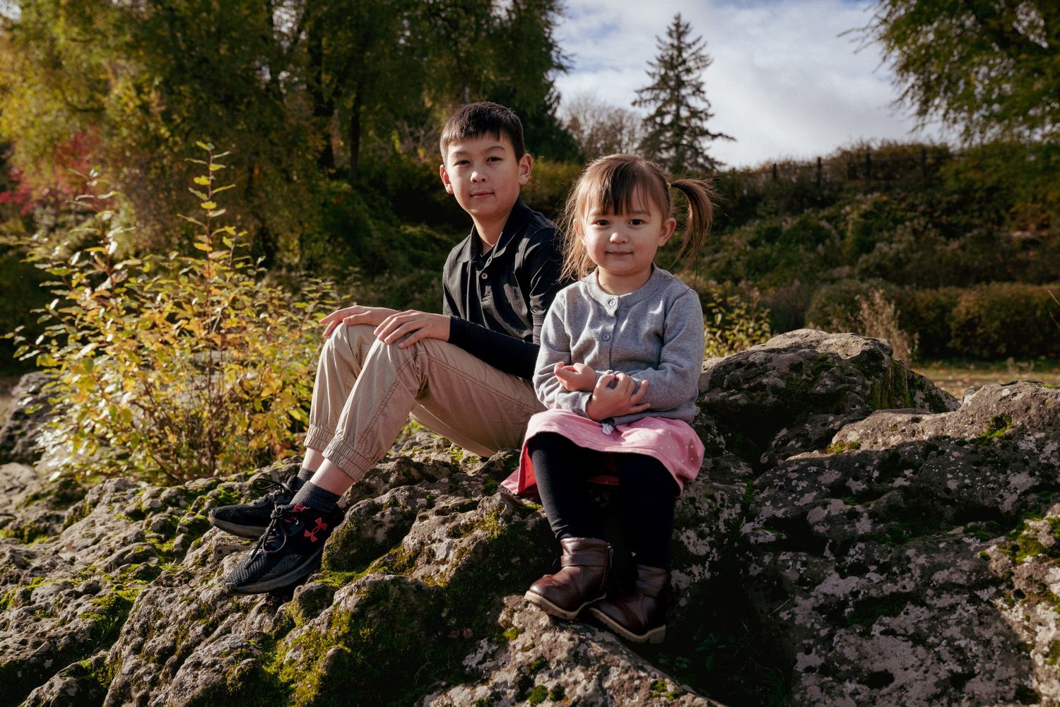 Brother and sister sitting on mossy rocks, forested area in Oregon, candid Pacific Northwest family moments.