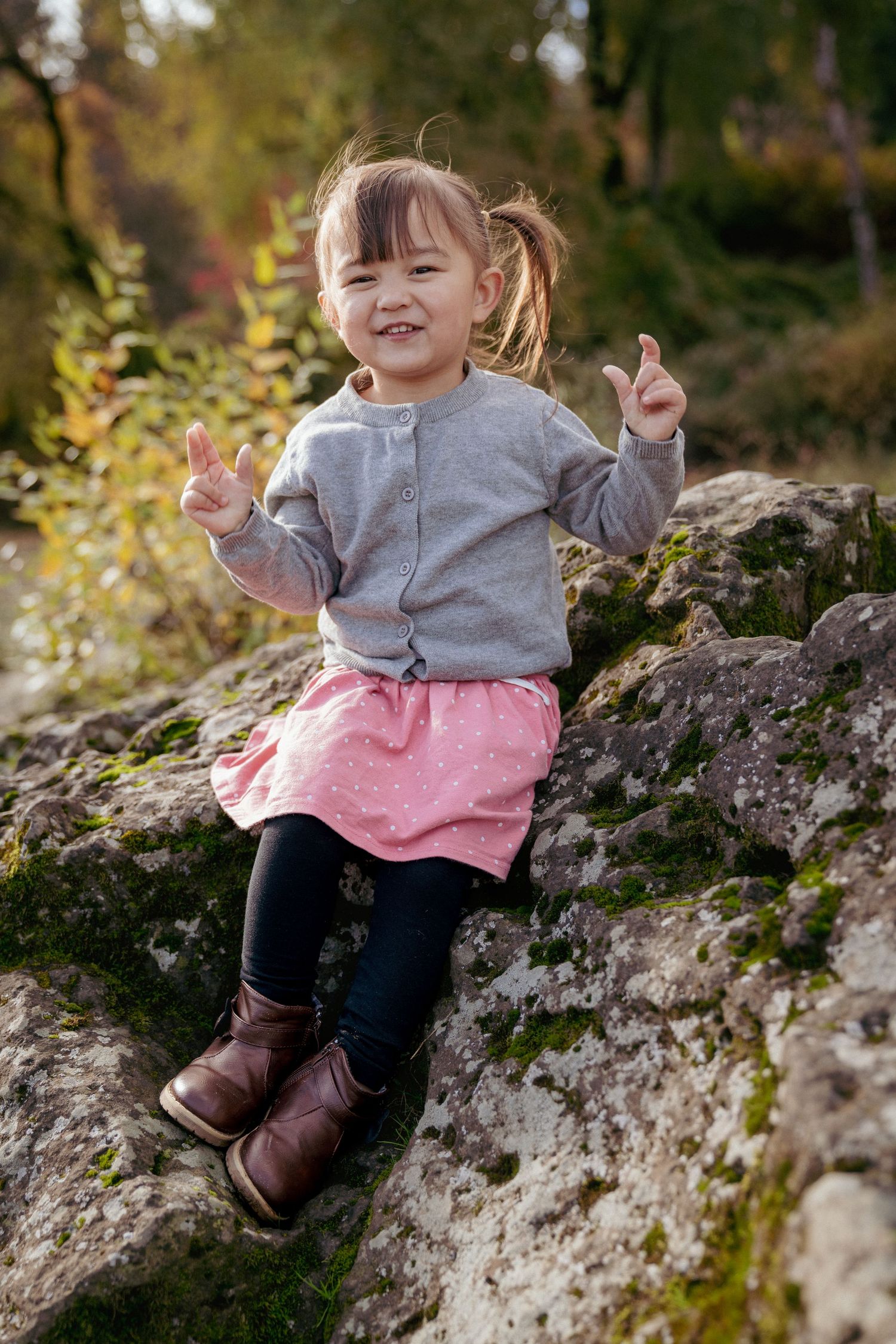 Toddler girl in pink skirt sitting on a mossy rock, fall family session in the Pacific Northwest, Oregon.