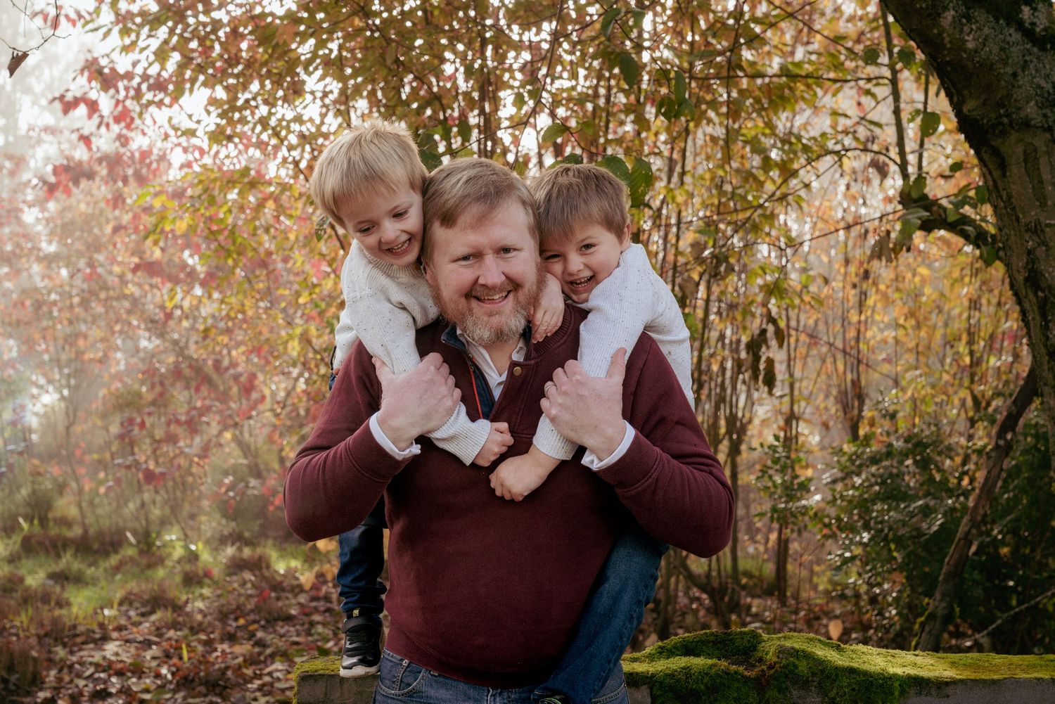 Laughing father with twin sons on his shoulders, fall family fun in Washington State park.