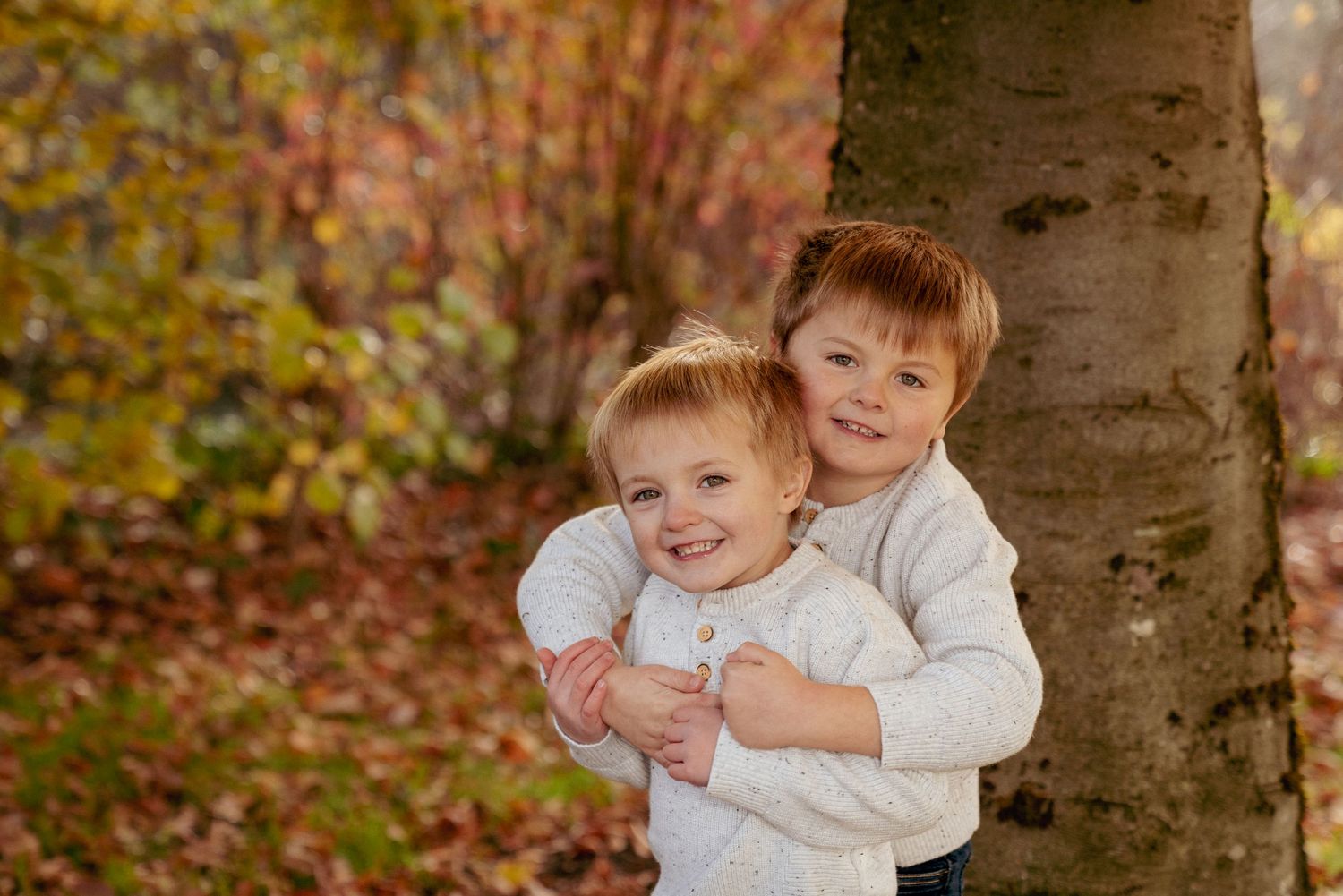 Adorable twin brothers hugging in autumn leaves, Oregon toddler photography, playful fall portrait session.