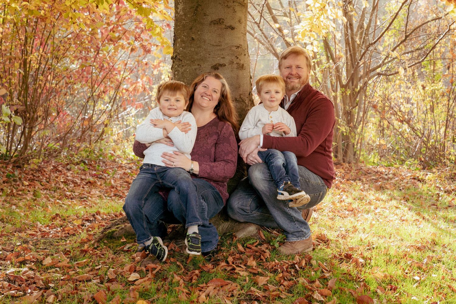 Cozy fall family photo with twins on leaf-covered ground, Oregon forest family session PNW.