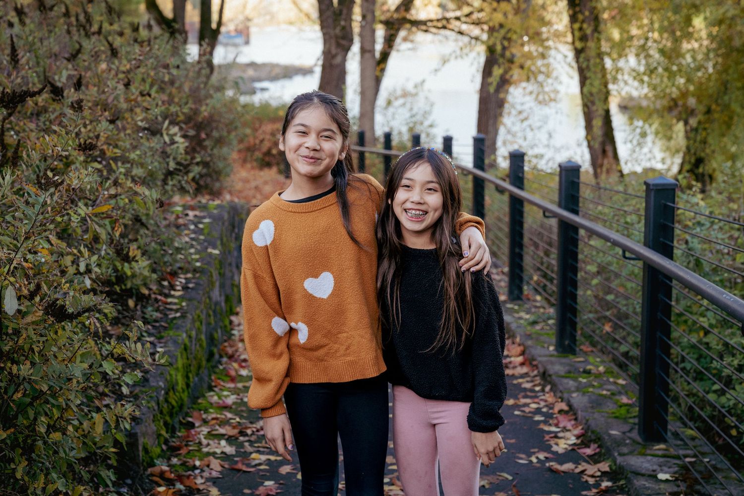 Sisters posing in cozy fall sweaters, vibrant autumn day in Portland metro area.