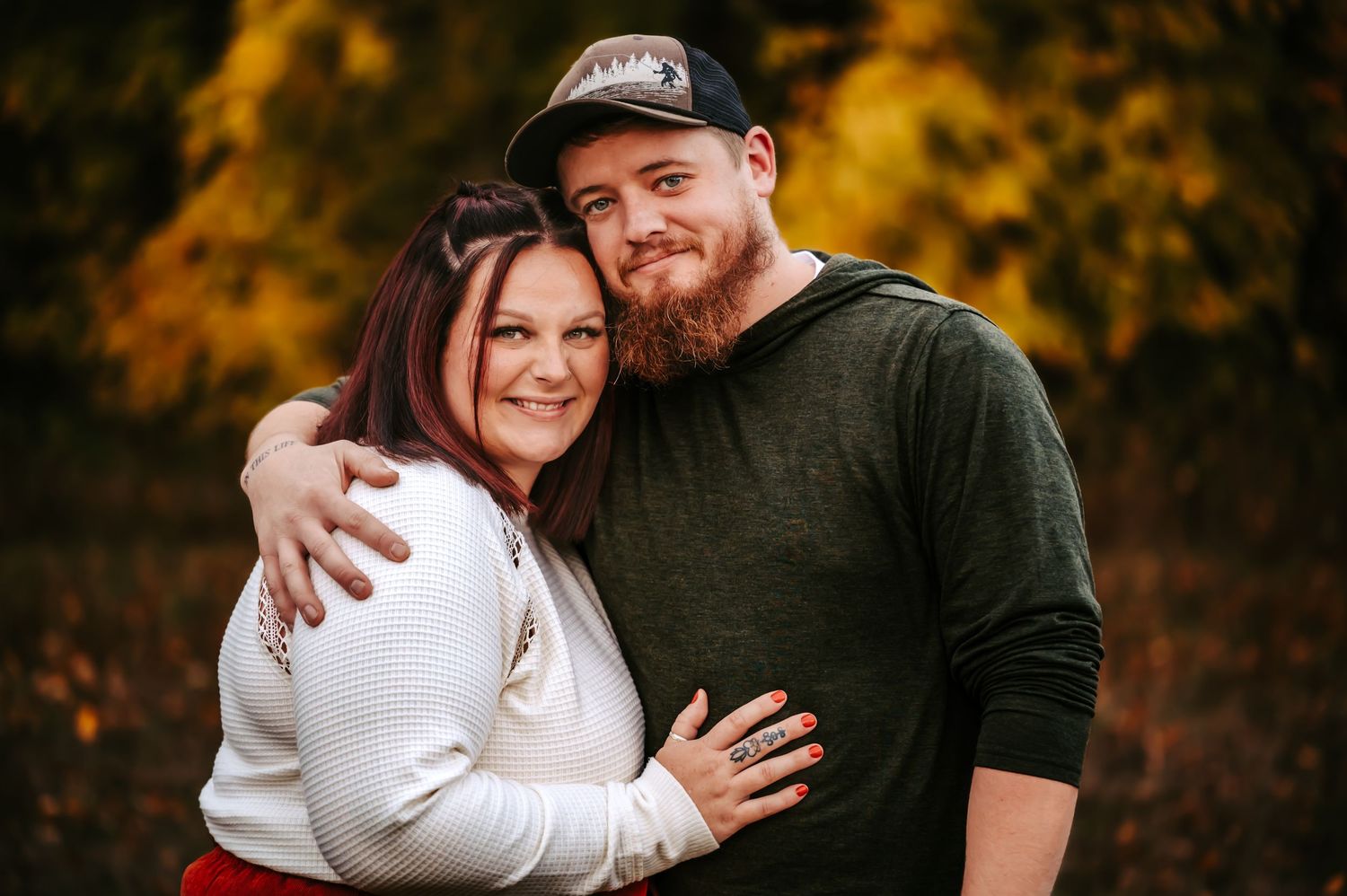 A couple embraces outdoors against a backdrop of golden autumn foliage in a romantic portrait session.