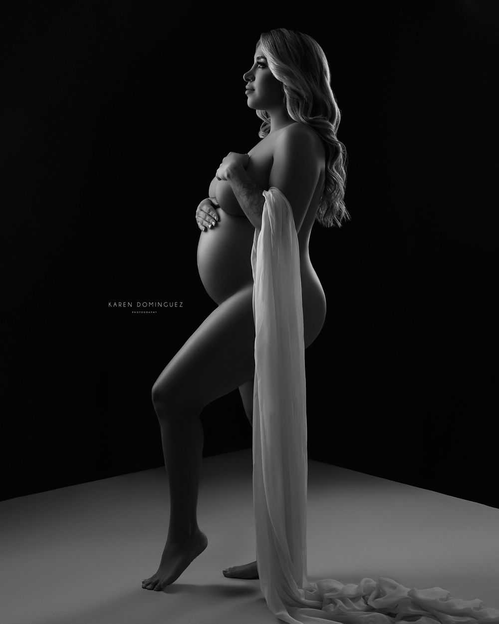 Dramatic black and white maternity silhouette with flowing fabric against dark background.