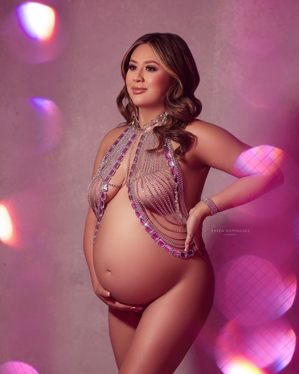 Maternity photo with feminine silhouette in sparkly halter top against pink bokeh lighting background.