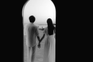 Silhouetted couple holding hands while standing in an arched doorway overlooking a scenic view.
