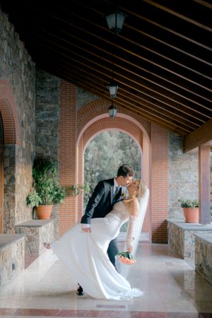 Romantic couple shares an intimate moment in a stone archway corridor decorated with terracotta brick and potted plants.