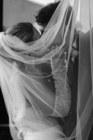 A romantic black and white wedding photo showing an intimate moment through a flowing bridal veil.