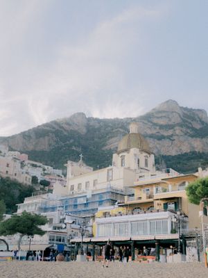 Colorful coastal buildings nestled against dramatic mountain backdrop on Mediterranean beach in Positano, Italy.