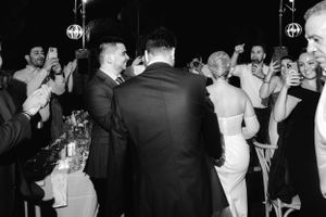 Black and white photo of people dancing and celebrating at an elegant party with hanging lights and formal attire.