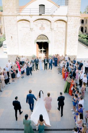 Wedding party enters historic stone church as guests line both sides of the walkway in formal attire.