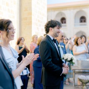 Wedding guests applaud during an outdoor ceremony as someone holds a white floral bouquet.