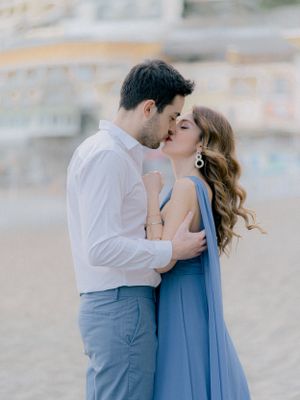 A romantic couple embraces in an intimate moment, with the woman wearing a flowing blue dress against a soft blurred background.
