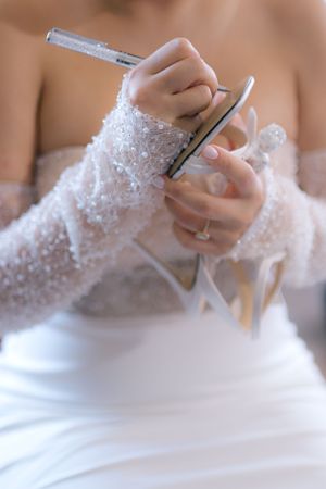 Close-up of delicate lace sleeve detail on a white wedding dress as hands hold a writing instrument.
