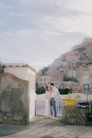 Two people stand on a terrace overlooking the colorful hillside buildings of Positano, Italy on a sunny day.